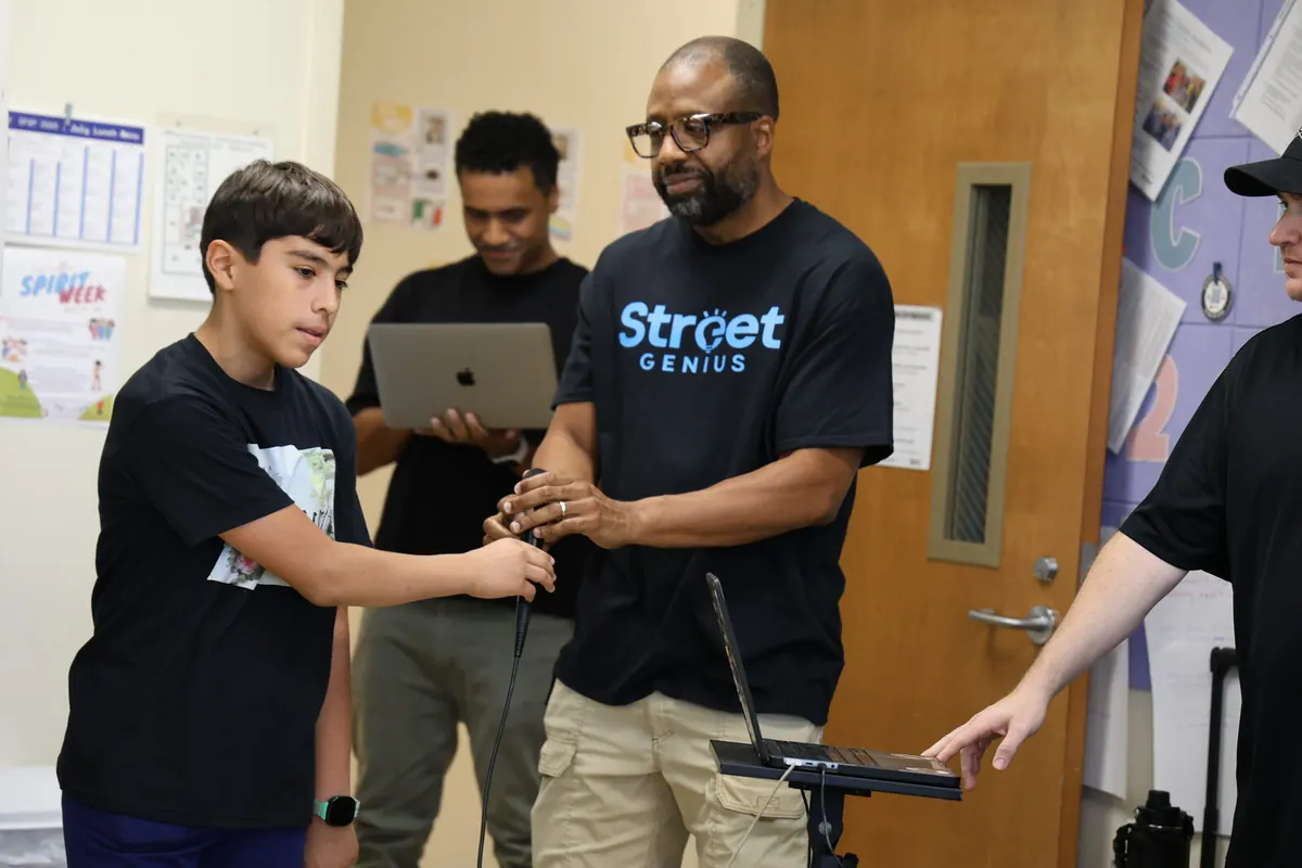 Bavu Blakes helps a young participant hold a microphone during a Street Genius activity.