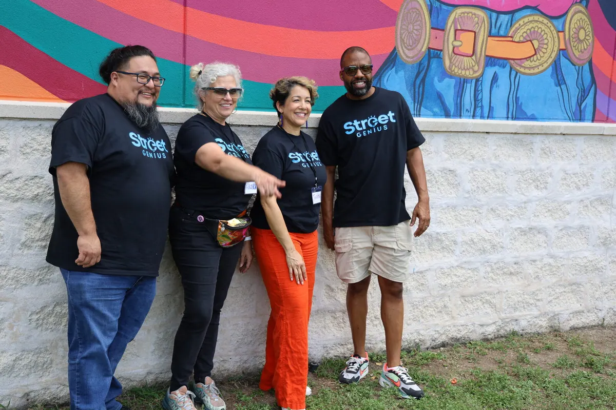 Bavu Blakes stands outside beside three Street Genius colleagues in front of a colorful mural.