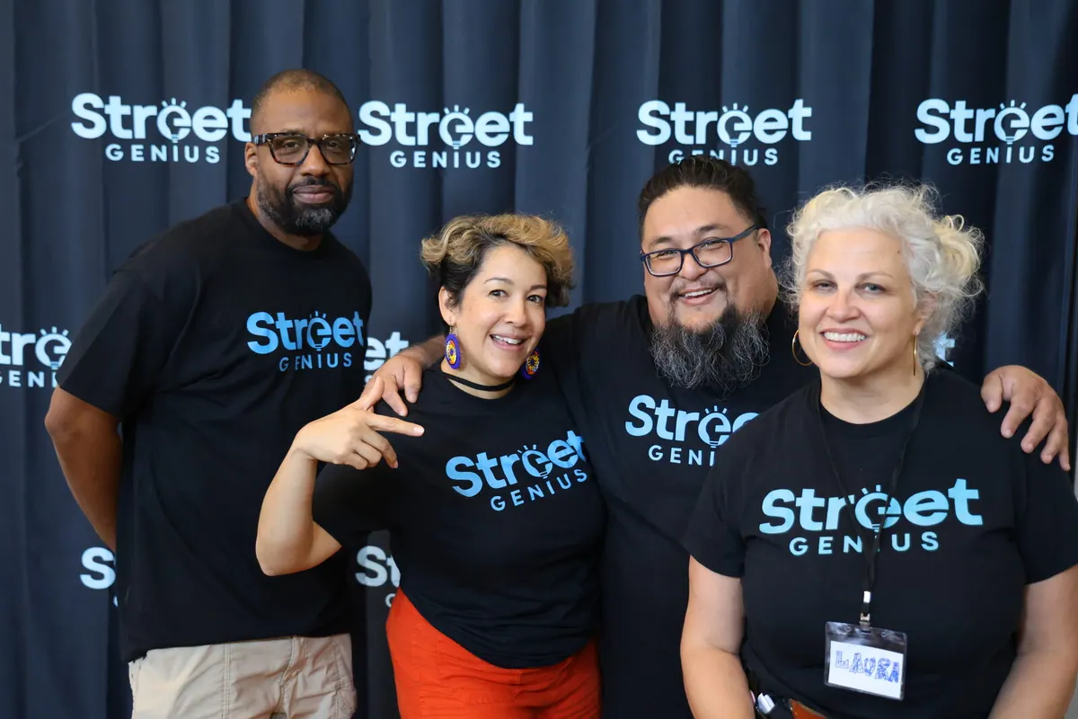 Bavu Blakes stands beside three Street Genius team members in front of a Street Genius backdrop.